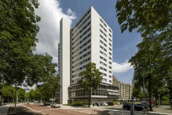 Hoog wit appartementencomplex aan de Van Leijenberghlaan, omgeven door bomen en geparkeerde auto's.
